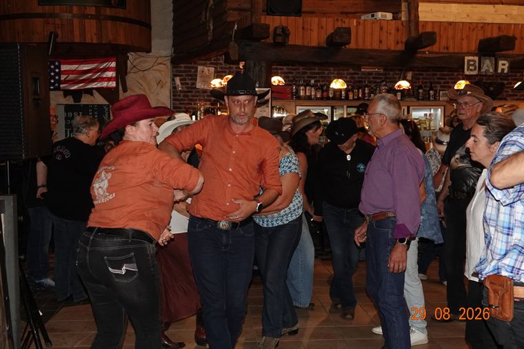 Line-dancers in oranje hemden op de dansvloer voor de bar
