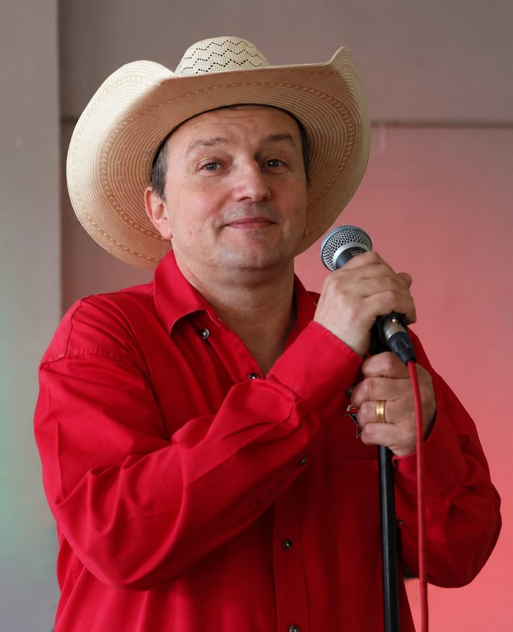 Patje Stew in rood hemd met lichte cowboyhoed, met microfoon in de hand