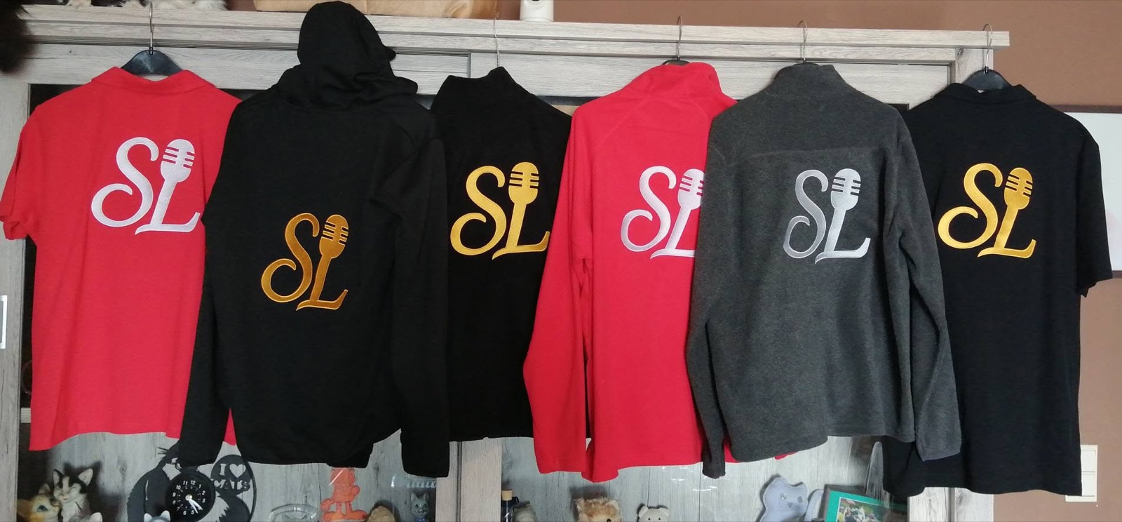 Zes kledingstukken met het geborduurde Stew Live Entertainment logo: polo's, hoodies en fleeces in rood, zwart en grijs